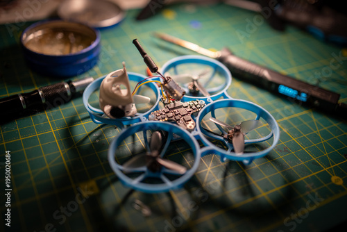 Tiny FPV whoop drone on a workbench during VTX repair, with exposed electronics and soldering probe.
