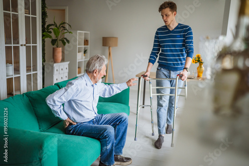 Картината върху платно Senior man experiencing back pain at home with caregiver bringing walker
