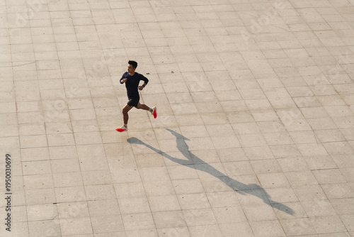 Solo male runner with long shadow on paved ground aerial top view outdoor