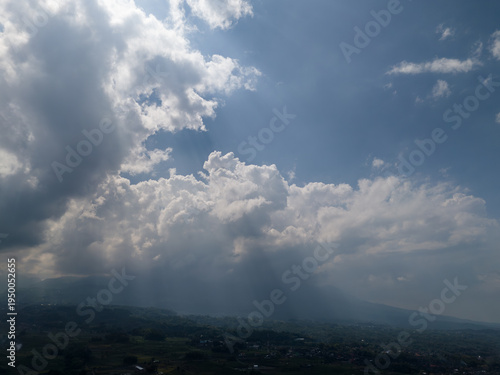 Dramatic sun rays breaking through clouds over the misty valley of Mount Lawu slopes.