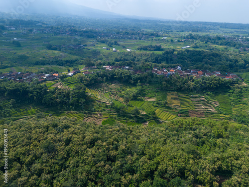 Aerial view of terraced rice fields and a small rural village in a lush green tropical valley.