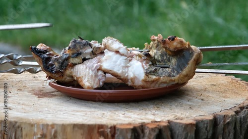 Taking cooked catfish fillet off skewers onto a plate on a wooden stump.