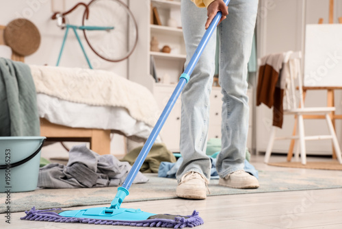 Teenage girl mopping floor in messy bedroom