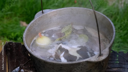 Close-up of fresh fish and whole onion boiling in a metal cauldron over an open fire, top view.