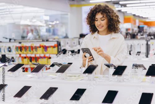 Woman shopping for a new smartphone, examining models on display in an electronics retail store