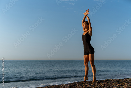 Tableau sur toile Fit woman stretching with raised arms on beach at sunrise, practicing mindful mo