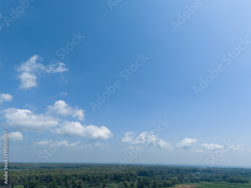 High angle perspective of vast blue sky and fluffy clouds over tropical teak forest landscape.