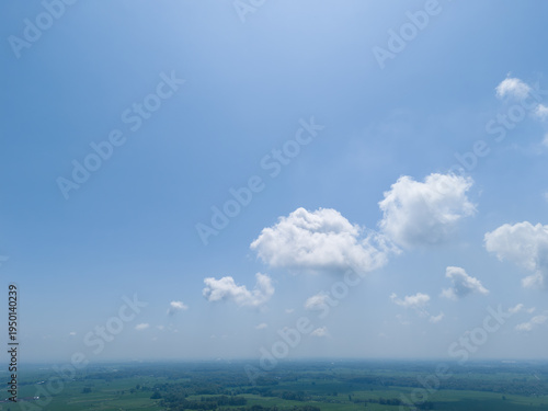 High angle perspective of vast blue sky and fluffy clouds over tropical teak forest landscape.