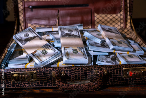 Large amount of cash stacked in a suitcase on a wooden surface in a dimly lit room
