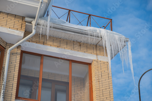 Icicles hanging from the roof of a building on a sunny winter day in a city