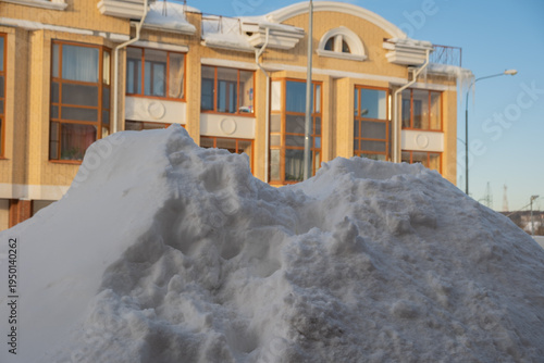 Large pile of snow near a building during winter in a city with clear blue sky and sunshine