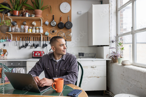 Young man planning his future working on a laptop in a kitchen