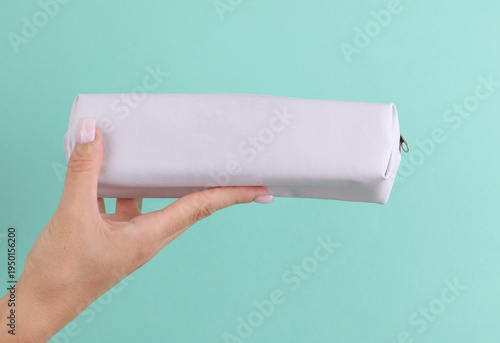 Woman's hand holds a white pencil case mockup on a mint-colored background