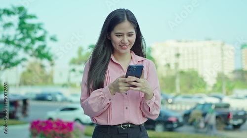 Smiling young woman talking on a smartphone outdoors in an urban area, expressing friendly communication, mobile connectivity, and modern digital lifestyle.