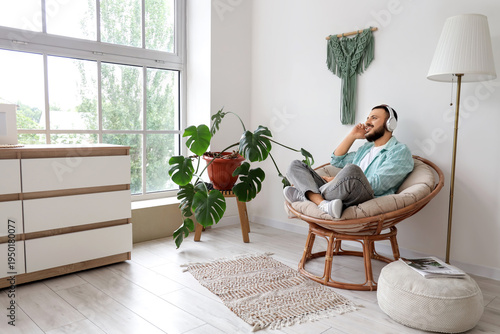 Handsome man with headphones listening to music in cocoon chair at home