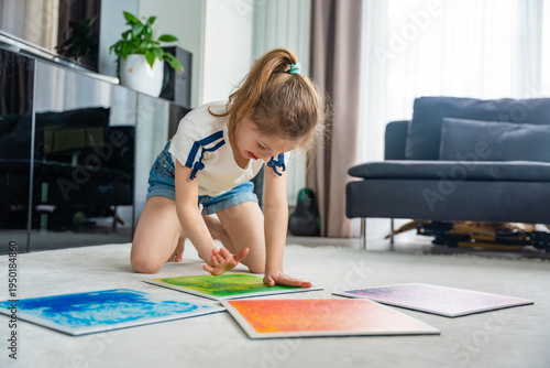 Quadro su tela Little girl kneeling on floor pressing colorful sensory gel mats with hands during play activity