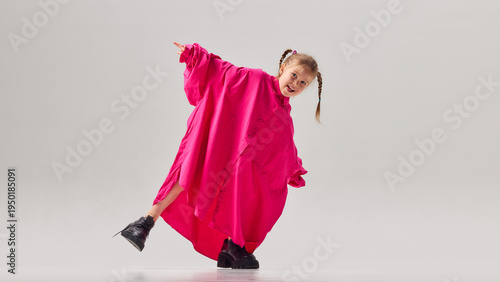 Φωτογραφία Little girl in oversized pink shirt and large shoes posing playfully in studio