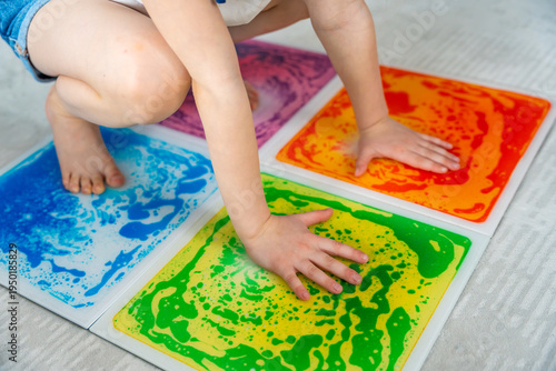 Little girl pressing colorful sensory gel mats with hands and feet while playing on floor. Sensory integration and motor development concept for autism support and occupational therapy activity.