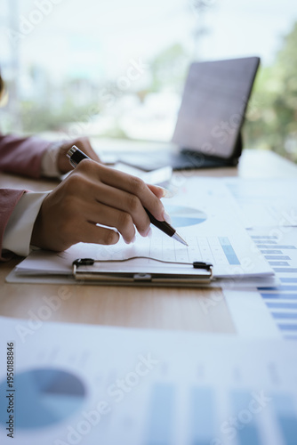 Fotografie A businesswoman analyzing financial charts and documents while using a calculator, focusing on data review and financial planning in a professional office setting
