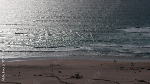 Aerial view of kitesurfers riding the waves near Guincho Beach, where golden sands meet the shimmering ocean, creating a vibrant coastal scene, Cascais, Lisbon, Portugal.