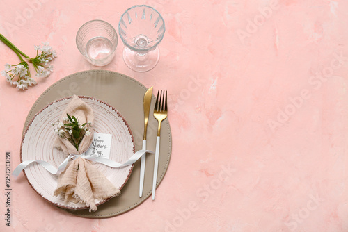 Stylish table setting with greeting card and beautiful flowers on pink background. Mother's Day celebration