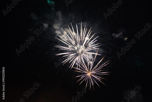  Beautiful white and golden fireworks bursting in the dark night sky during a celebration. Festive firework display with bright sparks and smoke against black background 