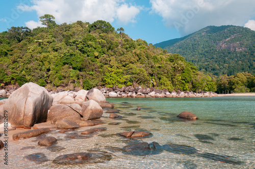 Rocky tropical coast with granite boulders in turquoise sea and lush rainforest hills at Tioman Island, Malaysia, natural island beach landscape.