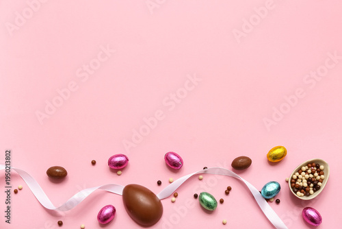 Chocolate Easter eggs in foil with candies and ribbon on pink background