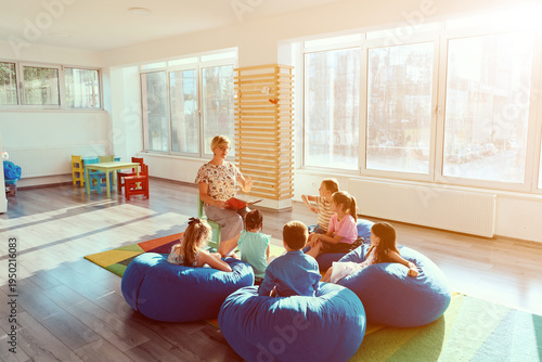 Teacher reading aloud to preschool children during story time in bright modern classroom
