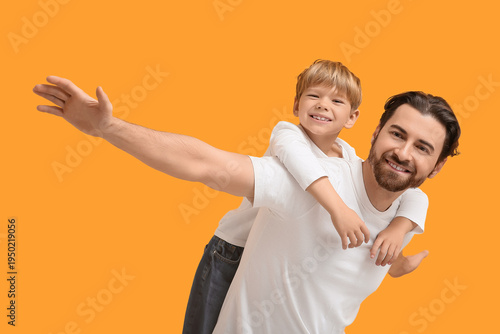 Little son riding his dad piggyback on yellow background. Father's day