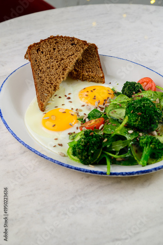 Breakfast plate with eggs, spinach salad, and brown bread on marble table