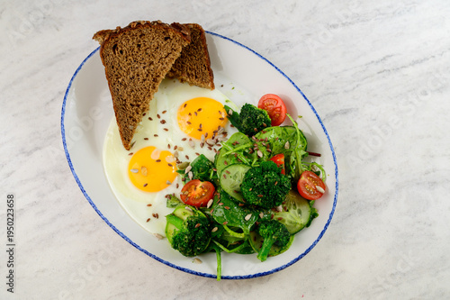 Breakfast plate with fried eggs, salad, and whole grain bread