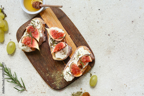 Wooden board of delicious fig bruschetta with ricotta cheese and bowl of honey on white background