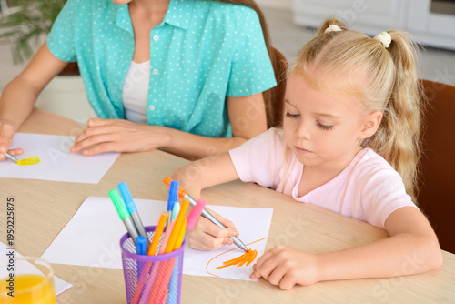 Cute little girl with nanny drawing at table in kitchen