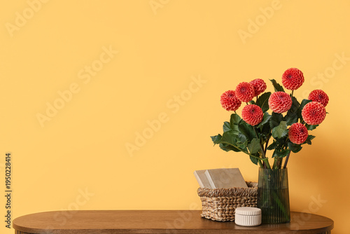 Vase with beautiful orange dahlia flowers on chest of drawers against yellow background