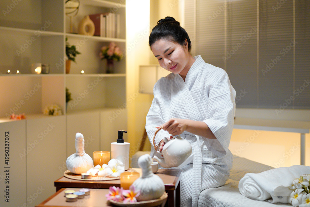 Fototapeta premium Beautiful young woman in white robe relaxing after spa procedures in oriental spa resort, drinking tea. Elegant woman relaxing, finding inner peace and balance