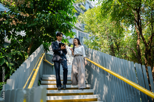 Business colleagues businessman and woman sitting and discussing,planning work using tablet outside office.City meeting and laptop with business people outdoor urban and green area for collaboration