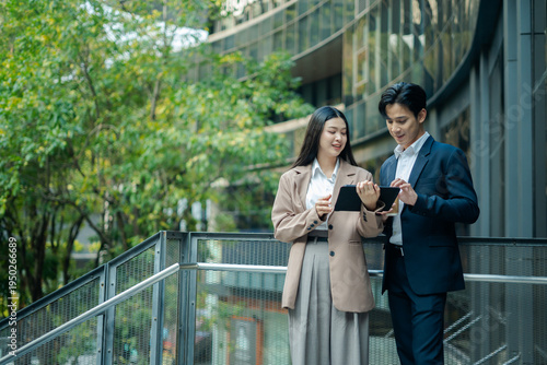 Business colleagues businessman and woman sitting and discussing,planning work using tablet outside office.City meeting and laptop with business people outdoor urban and green area for collaboration