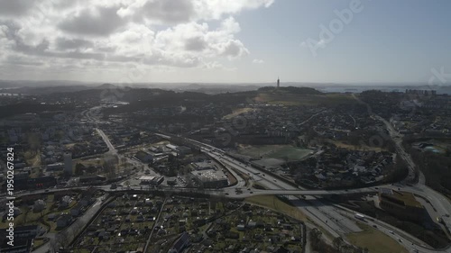 Aerial drone footage showing vehicle traffic moving along roads during midday under partly cloudy weather conditions. The scene captures cars, road infrastructure, and surrounding urban environment in