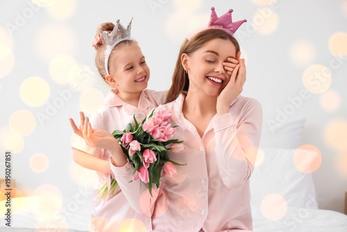 Cute little girl greeting her mom for Mother's Day with tulips in bedroom