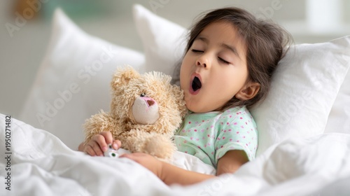 Sick child feeling unwell, yawning in bed with a teddy bear and a thermometer, recovering from illness