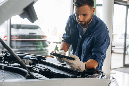 Wallpaper Mural Black digital tablet, hood is opened, fixing the automobile. Male mechanic is working in the modern car workshop Torontodigital.ca