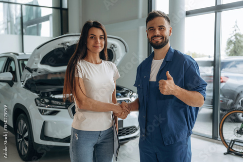 Deal, doing handshake. Woman customer is in the car repair service station with mechanic