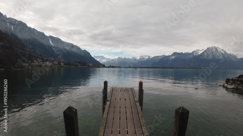 Person walking on wooden pier toward Alps on Lake Geneva in Montreux Switzerland