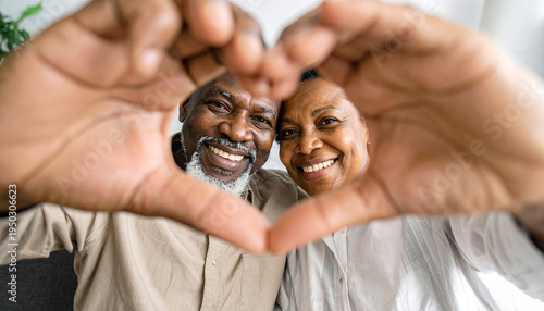 Seniorenpaar formt mit den Händen und Fingern ein Herz und schaut durch das Herz in die Kamera