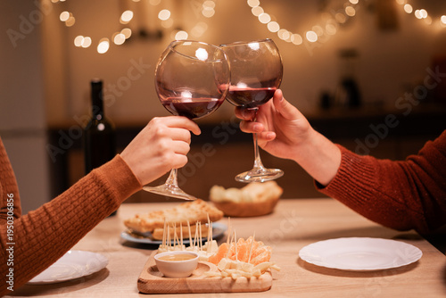 Cropped photo of couple clinking glasses of wine at home. Romantic dinner concept
