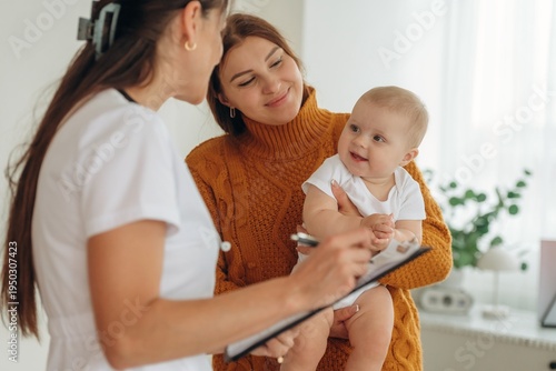 Using pen, writing information. Mother with her little baby daughter is in clinic with doctor at appointment