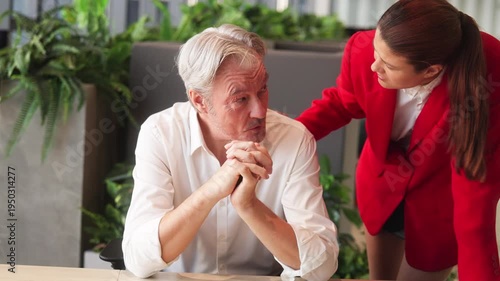 Young businesswoman encouraging senior colleague during discussion at office desk, showing teamwork, leadership support, and professional workplace collaboration.