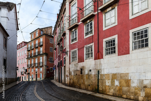 Narrow, cobblestone street in Lisbon, Portugal lined with colorful, old buildings in the historic Alfama neighborhood.