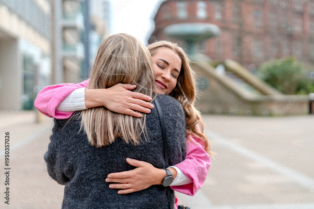 Fototapeta premium Two women share a hug in a city street during the morning